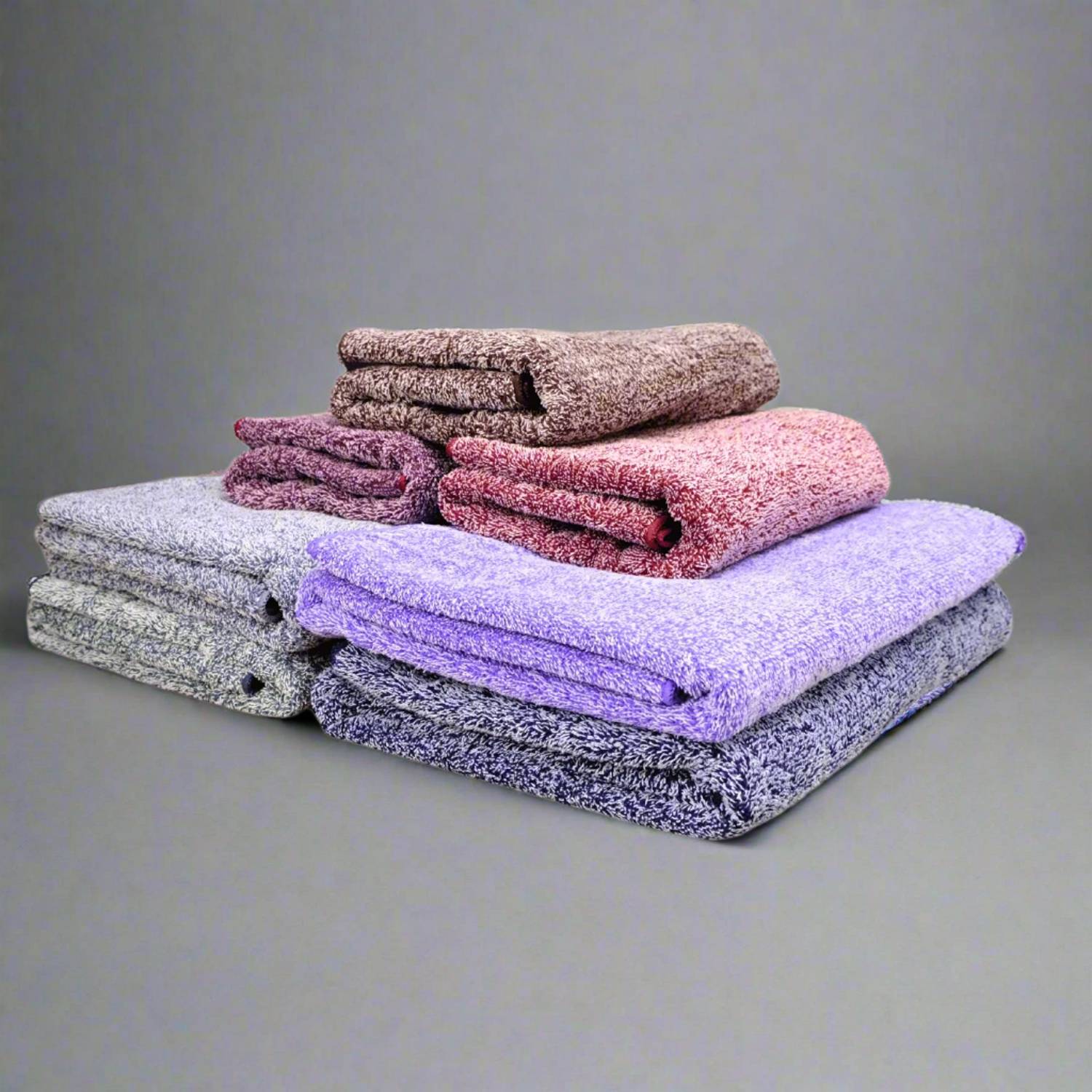 Stacked microfibre bath towels in various colors including white, brown, gray, and purple.