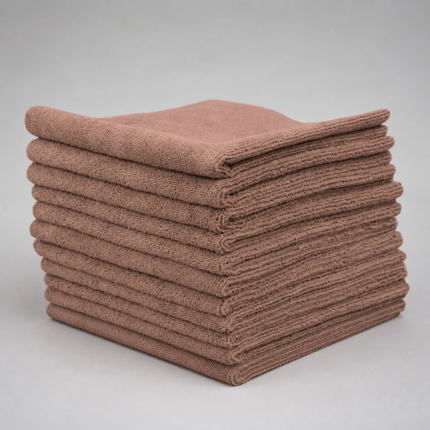 A stack of folded brown microfiber cloths on a neutral gray background.